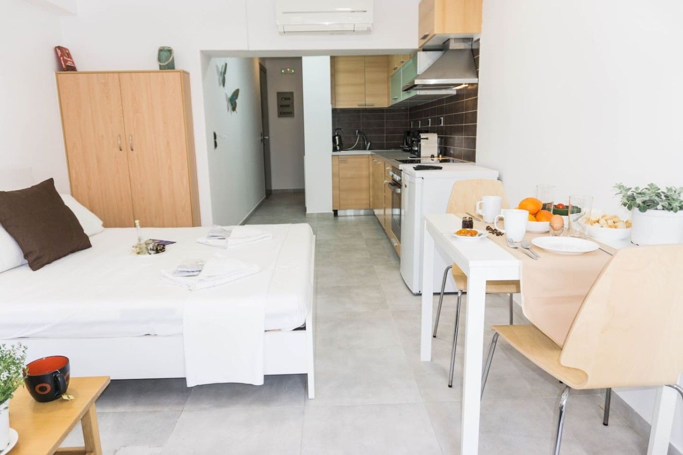 A modern hotel room with a bed, a dining table, and a kitchenette.