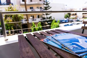 A wooden bench with magazines on it, overlooking a balcony with a view of buildings and parked cars.