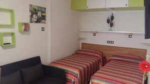 A bedroom with two beds, a black sofa, and green storage units.