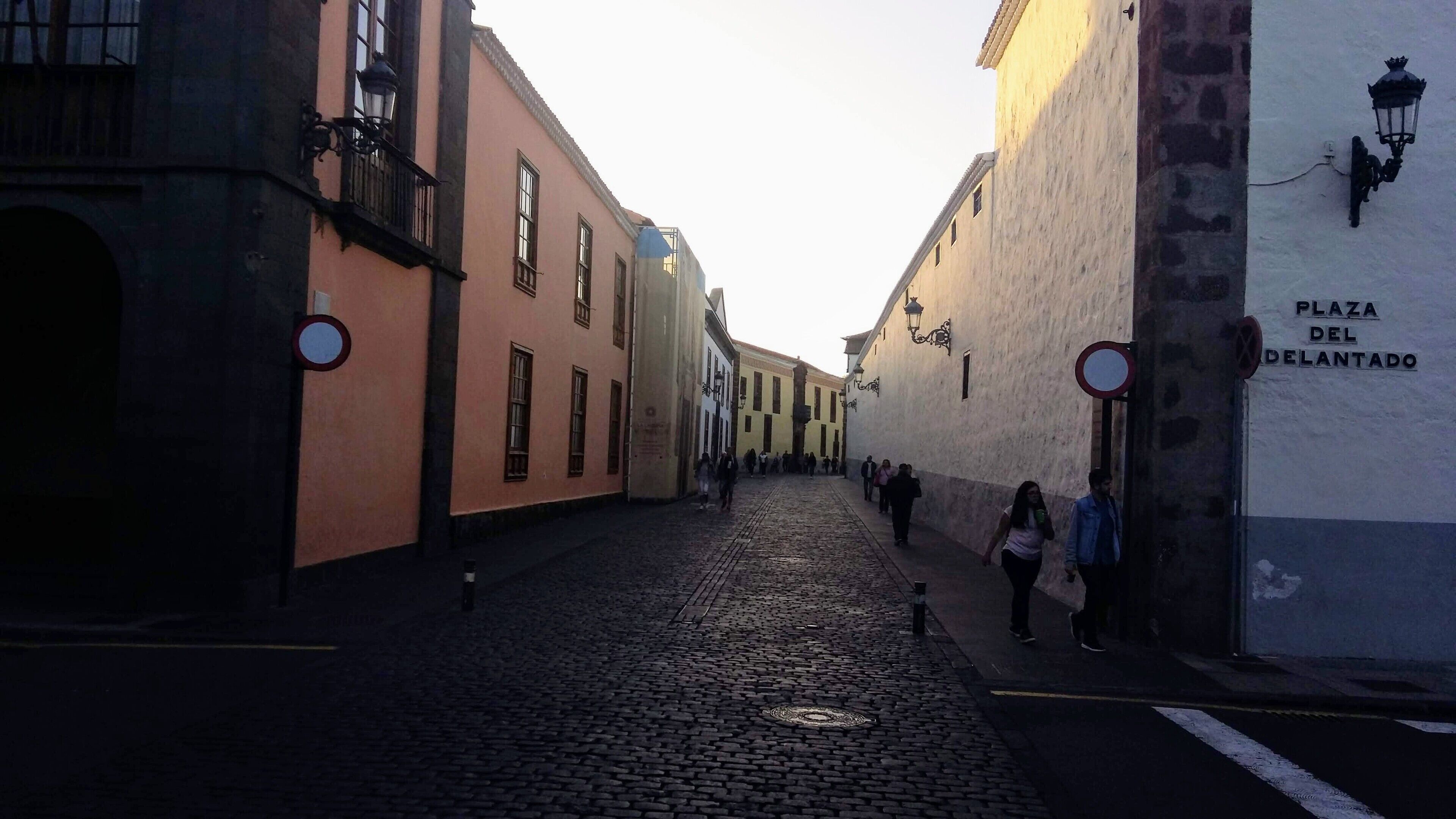 Calle adoquinada con edificios históricos, un cartel que indica Plaza del Planchado y peatones.