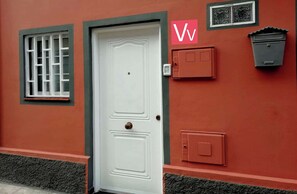 Une porte blanche avec une petite fenêtre au-dessus, une boîte aux lettres et une plaque numérotée fixée au mur.