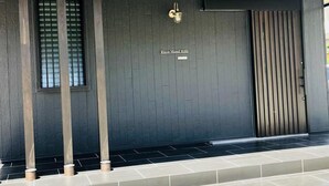 Une façade moderne avec un mur gris foncé, une enseigne indiquant « Ricco Mond Hills » et un portail métallique vertical.