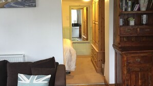 A living room with a brown sofa, a clock, and a bookshelf. - Well Cottage, a one bedroom self-catering holiday cottage all on one level. (Kent)