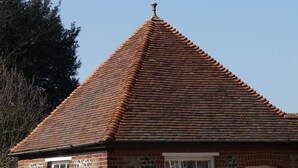 A small brick building with a tiled roof, a stone wall, a white door, and a table with chairs outside. - Well Cottage, a one bedroom self-catering holiday cottage all on one level. (Kent)