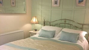 A neatly made bed with a patterned bedspread, a bedside lamp, and a wall-mounted mirror. - Well Cottage, a one bedroom self-catering holiday cottage all on one level. (Kent)