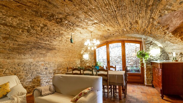 A rustic stone interior with a sofa, wooden dining table, and a view through a window. - Self catering Can Nentia for 9 people (Forallac)