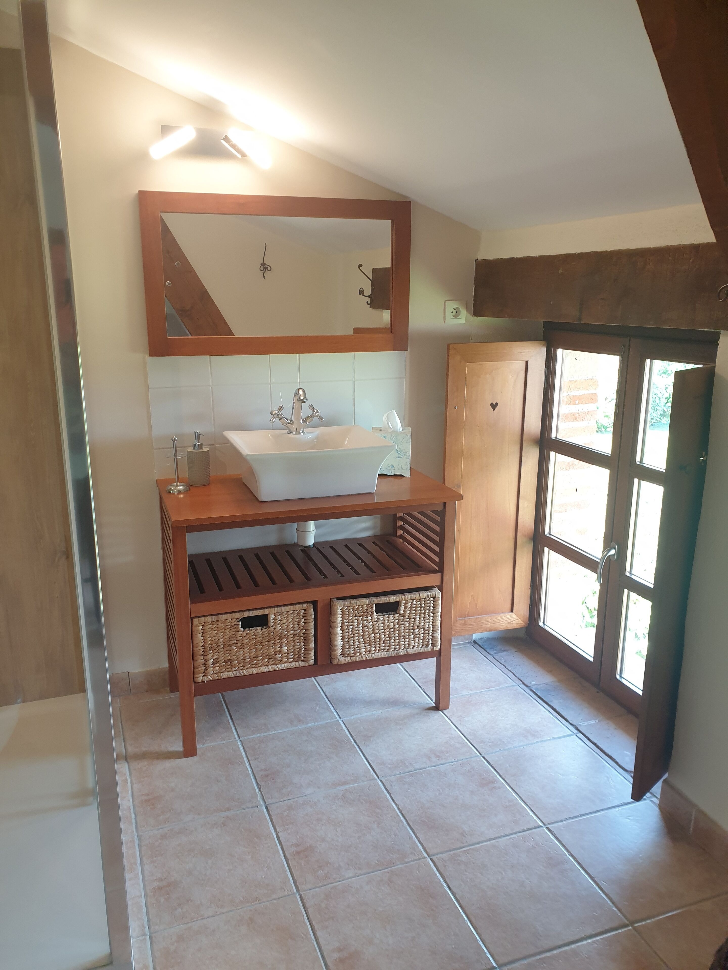 A bathroom with a wooden vanity, a white sink, a mirror, and a window.