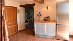 Une cuisine avec des meubles blancs, un réfrigérateur Bosch et une poutre en bois au plafond.