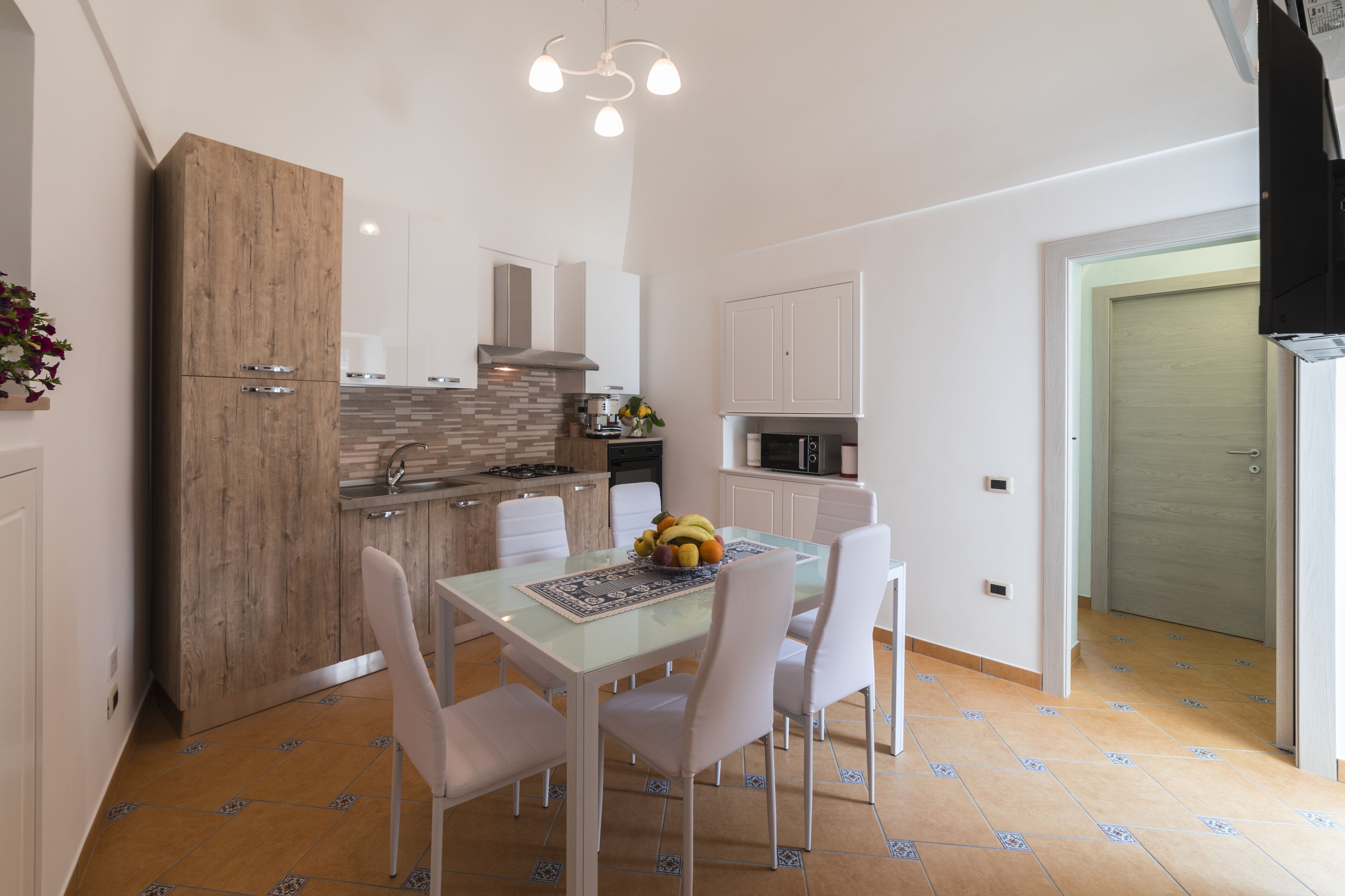 A modern kitchen with white cabinets, a wooden accent wall, and a dining area with a glass table and white chairs.