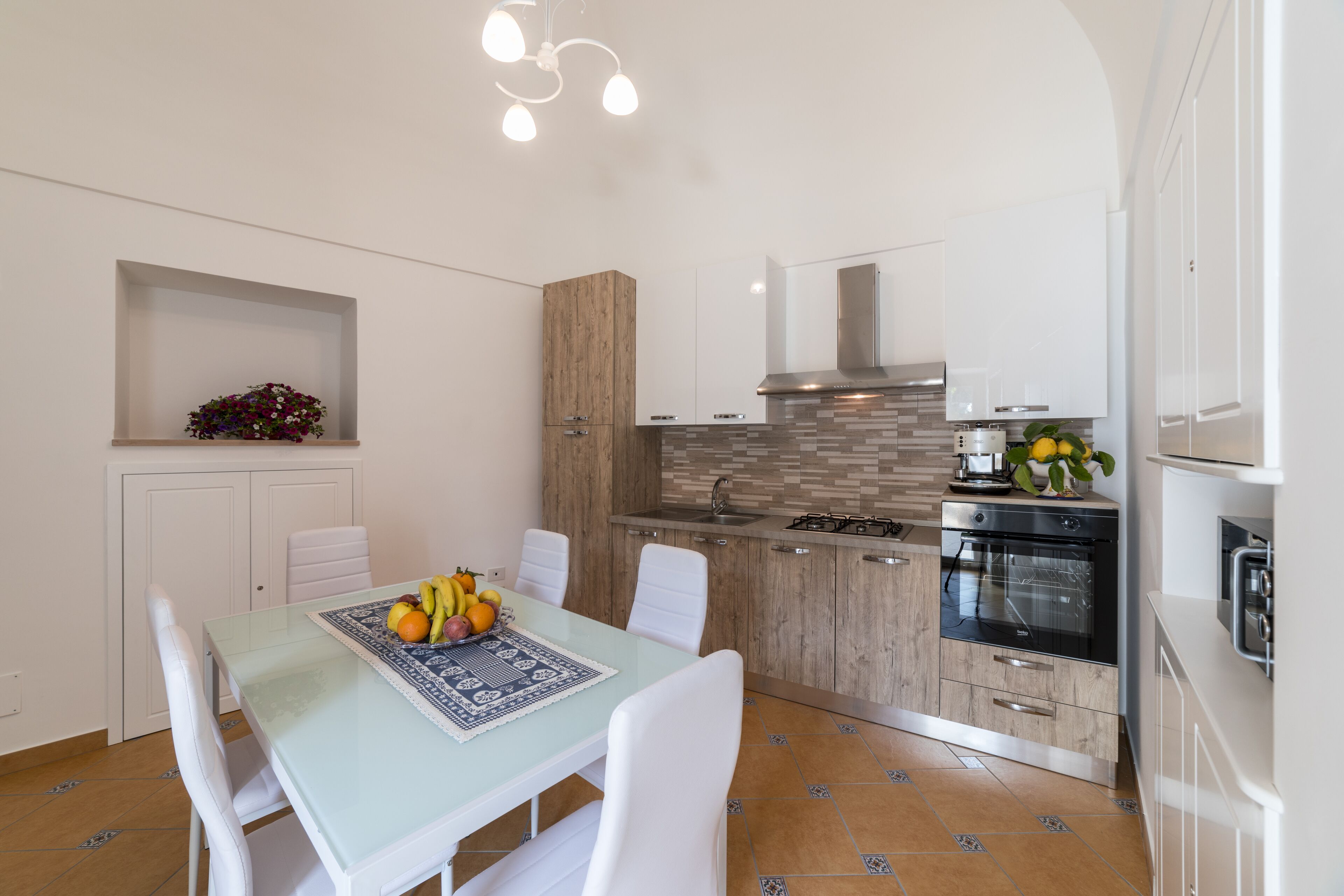 A modern kitchen with white cabinets, a wooden accent wall, and a dining area with a glass table and white chairs.