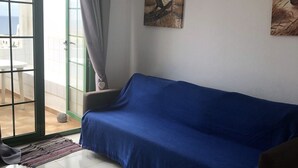 Un soggiorno con un divano blu, un tappeto piccolo e vista su una zona esterna attraverso una porta in vetro.