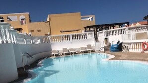 Una piscina con lettini, un galleggiante e una recinzione bianca.