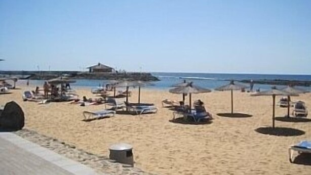 Una spiaggia con lettini e ombrelloni, un edificio sullo sfondo e cielo sereno.