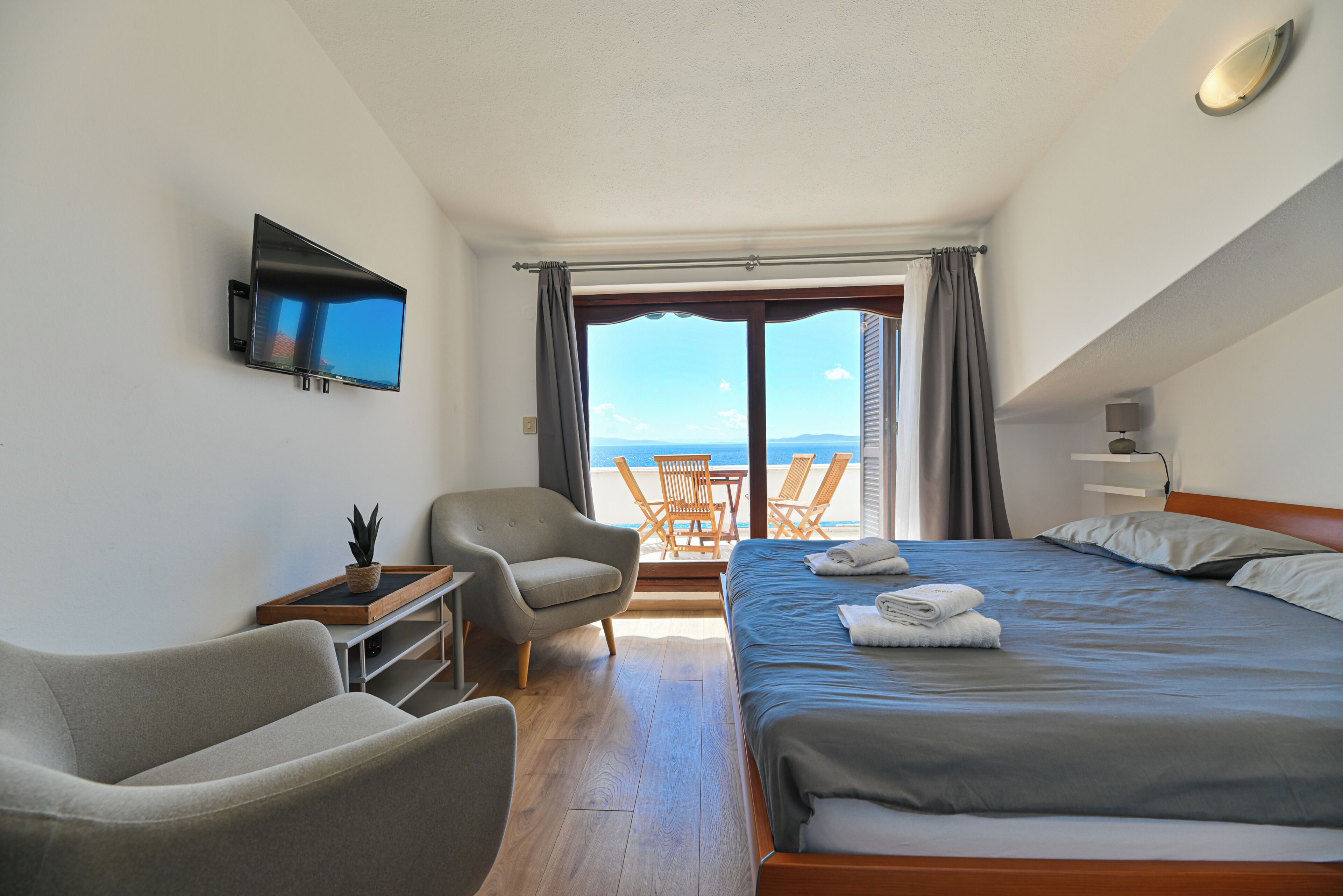 Ein Hotelzimmer mit einem Bett, zwei Sesseln, einem Fernseher, einem Tisch und Meerblick.