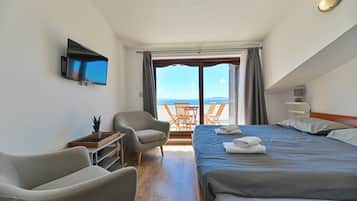Ein Hotelzimmer mit einem Bett, zwei Sesseln, einem Fernseher, einem Tisch und Meerblick.