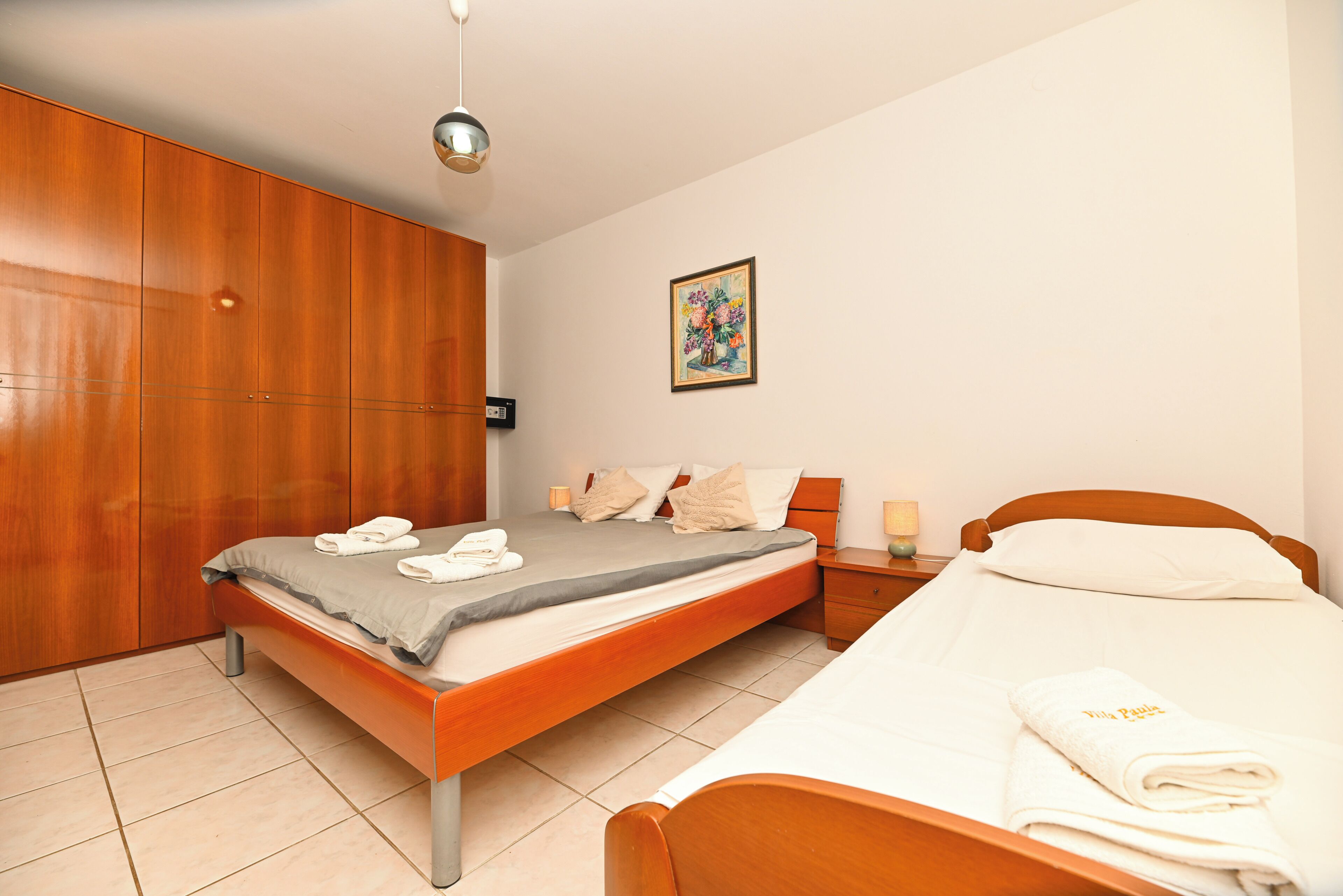 A bedroom with a bed, a wardrobe, a nightstand, and a wall-mounted painting.