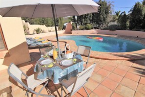 Ein Tisch am Pool mit Tischdecke, Stühlen und Sonnenschirm.