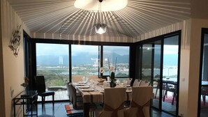 Un espace repas avec une table dressée pour six personnes, de grandes fenêtres offrant une vue sur le paysage urbain et un design de plafond moderne.