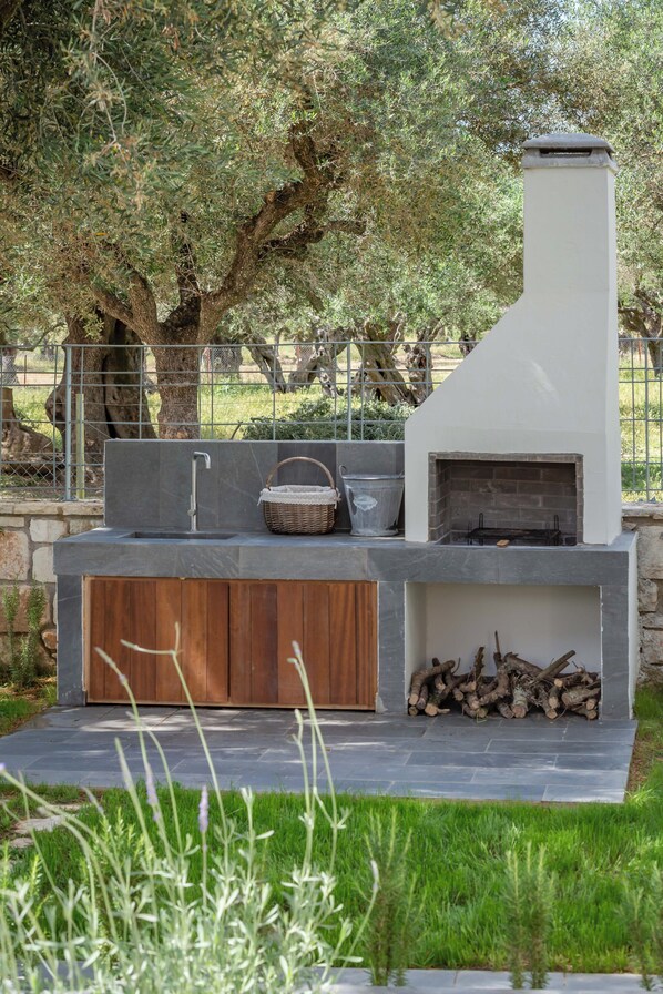 Una cocina al aire libre con encimera de piedra, un armario de madera y una chimenea de ladrillo.