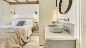 A bedroom with a large bed, a bedside table, and a nightstand. There is a bathroom with a sink, mirror, and towel rack. - Classic Three Bedroom Cottage with private pool (Zakynthos)