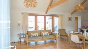 Un vaste espace de vie doté d’un plancher en bois, d’un ensemble de canapés, d’une table à manger et de deux lampes suspendues.