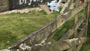Une clôture en bois avec une pancarte indiquant « Bryony Cottage », et une vue sur un chalet doté d’un toit en pente et d’un petit porche.