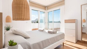 A bedroom with a bed, a bedside table with a plant, a hanging light fixture, and a view through a glass door. - Villa La Calma - beach,private Pool, free AC&WiFi (Es Mercadal)
