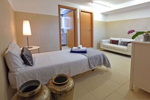 Ein Hotelzimmer mit einem Bett, einer Nachttischlampe, einem Sofa, einem kleinen Tisch und einer Vase mit Blumen.