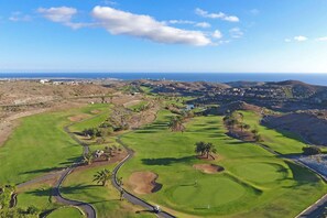 Ein Golfplatz mit freiem Blick auf das Meer, einer kurvenreichen Straße und einigen Gebäuden in der Ferne.