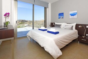 Ett modernt hotellrum med en stor säng, ett skrivbord och utsikt över landskapet genom glasdörren.