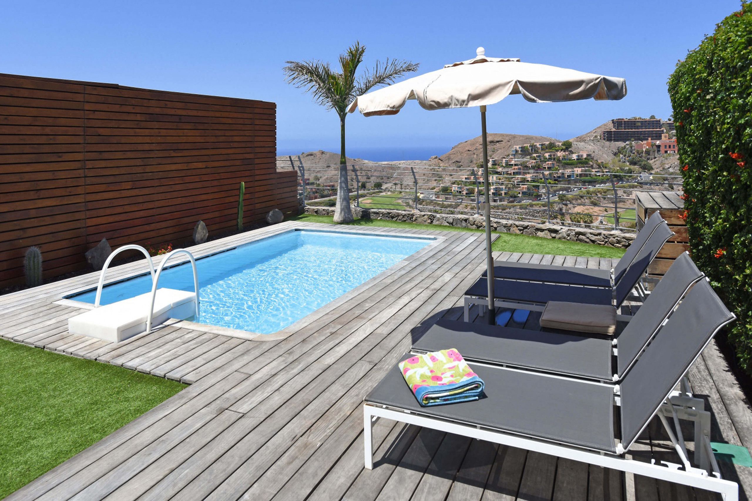 A wooden deck with a pool, lounge chairs, and an umbrella.