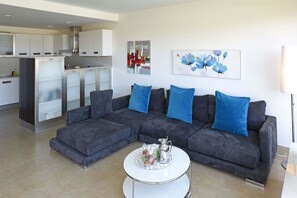 A modern living room with a grey sectional sofa, a white coffee table, and a kitchen area in the background.
