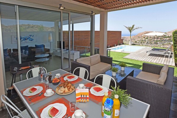 A modern outdoor dining area with a view of the pool and hills.