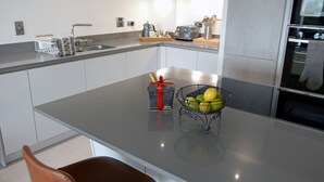 A modern kitchen with a stainless steel countertop, a bowl of fruit, a gift box, and a coffee maker. - Apartment 2 Waterstone House - Sea View Apartment (Tenby)