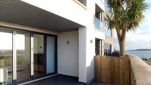 A modern apartment with a sliding glass door leading to a living area, a wooden deck, and a view of the sea. - Apartment 2 Waterstone House - Sea View Apartment (Tenby)