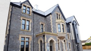 A stone building with multiple windows and a central entrance with an archway. - Apartment 2 Waterstone House - Sea View Apartment (Tenby)