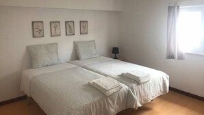 En dubbelsäng med två kuddar, en sänglampa och ett fönster med gardiner.