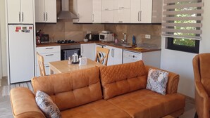 Eine moderne Küche mit weißen Schränken, ein Essbereich mit einer braunen Ledersofa und ein Fenster mit Jalousien.