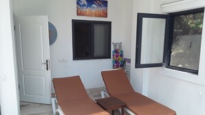 Ein Zimmer mit zwei Liegestühlen, einem kleinen Tisch, einem Fenster und einer Tür.