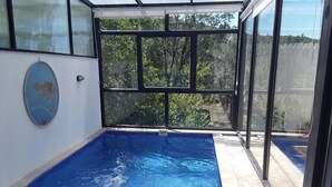 Ein Schwimmbad mit Glasüberdachung, umgeben von einer gefliesten Terrasse.