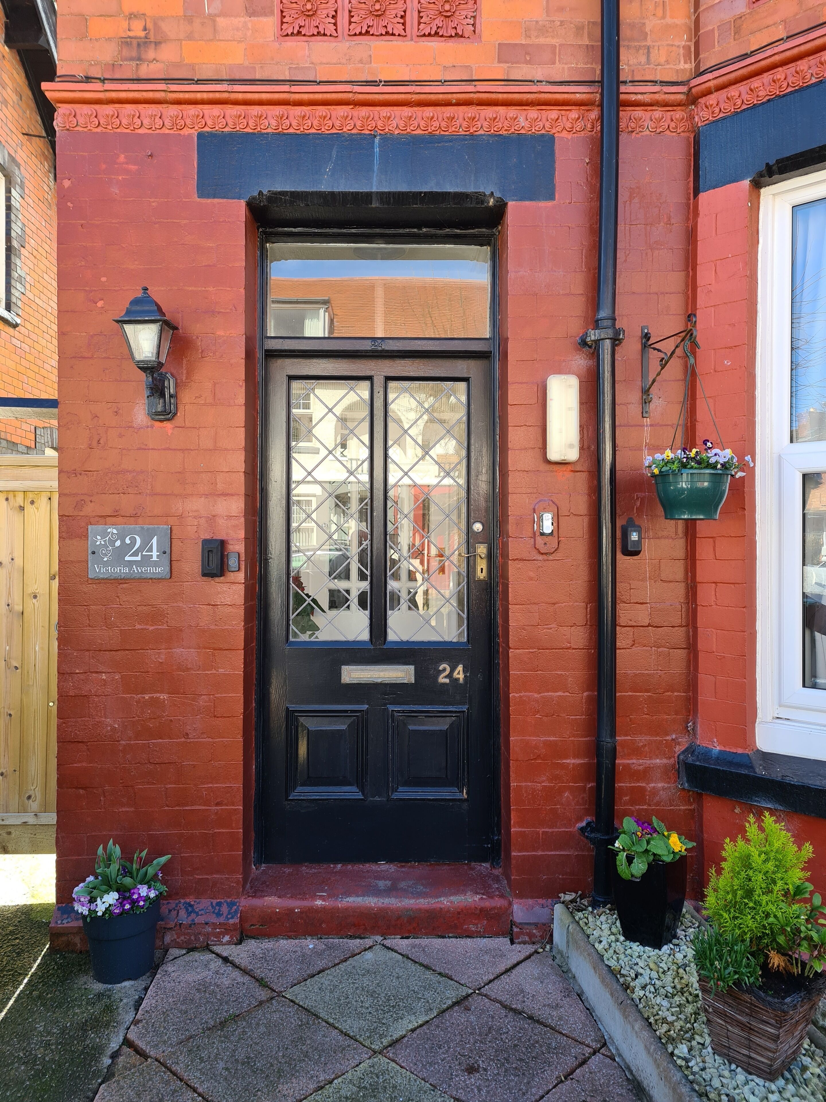 A black double door with the number 24, a small window above it, and a flower pot on the right.