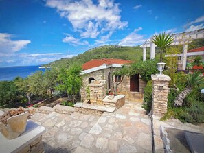A stone building with a red-tiled roof, a stone staircase leading to a door, and a view of the sea in the background. - Apartment"View Lux"-sea view,swimming pool, jacyzzi, sauna,garden,playground (Vela Luka)