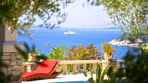 A poolside view with a lounge chair, a stone balustrade, and a view of the sea with a ship. - Apartment"View Lux"-sea view,swimming pool, jacyzzi, sauna,garden,playground (Vela Luka)