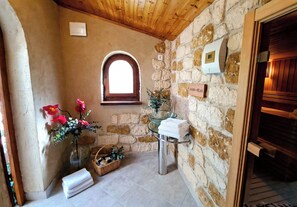A stone-walled bathroom with a wooden ceiling, a small window, a glass sink, and a towel rack.