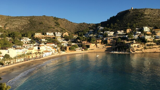 A coastal town with buildings on a hillside, a beach, and a calm sea. - Detached 2 Bedroom Villa in El Portet, with large terraces and pool views (Teulada)