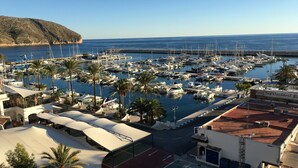 A marina with numerous boats docked, surrounded by palm trees and buildings with flat roofs. - Detached 2 Bedroom Villa in El Portet, with large terraces and pool views (Teulada)