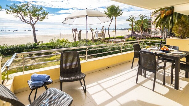 A balcony with a table set for dining, overlooking a beach with boats and palm trees. - Cosy apartment for 4 people with WIFI, A/C, TV and patio (Alcúdia)