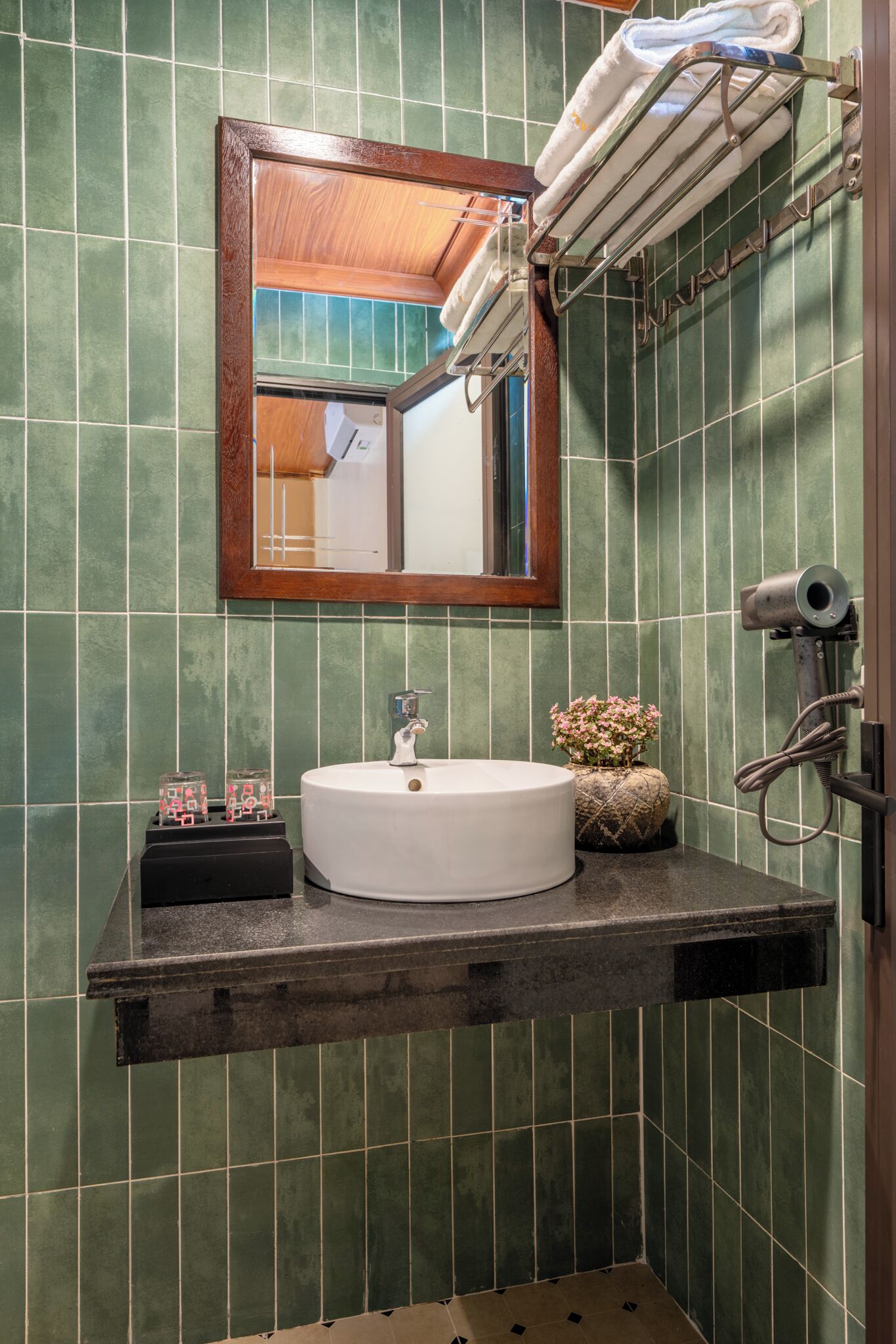 A bathroom with a white sink, green tiled walls, a wooden-framed mirror, and a towel rack.