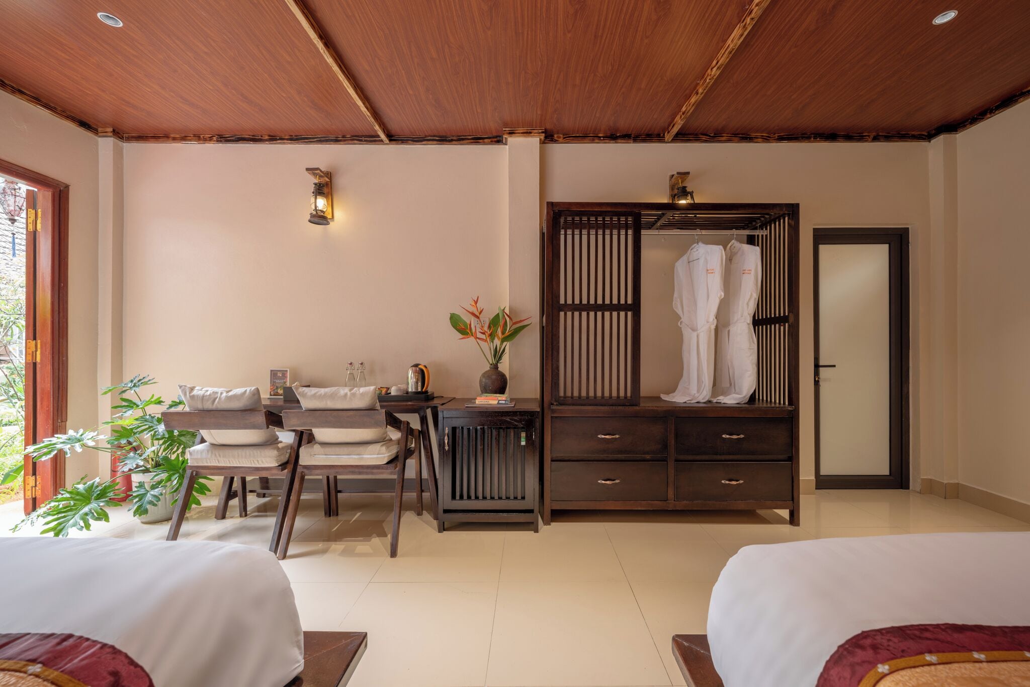 A hotel room with a wooden ceiling, a bed, a desk with a chair, a wardrobe, and a large window.