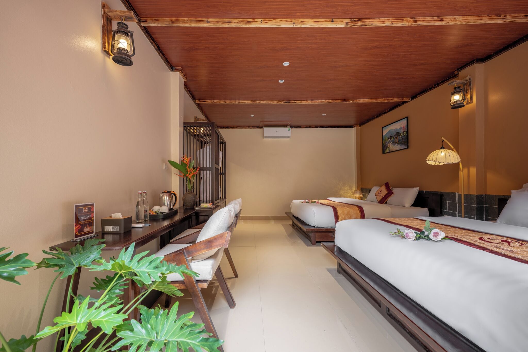 A hotel room with two beds, a desk, a chair, and a potted plant.